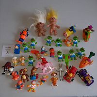 Photo showing full assortment of toy figures including Muppets, trolls, Garfield, and other cartoon characters, arranged flat on table.