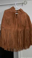 Full view of brown suede poncho with long fringe hanging from hem and chest front.