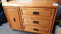 Front view of wooden dresser showing three drawers with dark metal pulls and left cupboard door closed