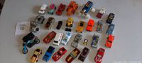 Top-down view of all 28 vintage toy cars and motorcycles arranged in rows showing size and color variety.