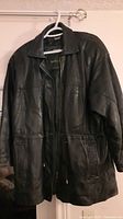 Front view of the black leather jacket hanging, showing overall condition and style.