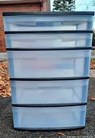 Front view of the plastic storage unit showing all five translucent drawers and black frame.