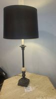 Full view of tall black metal table lamp with black lampshade, marble ball accent, and heavy base on a table.