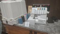 Photo showing Brother Lock 1034D overlock serger machine, several spools of thread, foot pedal, and white hard plastic carrying case.