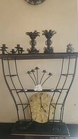 Wrought iron shelf unit with assorted candle holders and Del Sol ceramic sun clock placed centrally below shelf