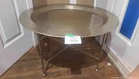 Round hammered metal tray top coffee table on metal stand with double cross bars. The stand is foldable for transport or storage.