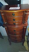 Front view of the tall polished wooden jewelry box with multiple drawers and side columns