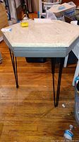 Hexagon shaped marble top table with three legs each having three black poles, showing the full table including legs and top, on wooden floor.