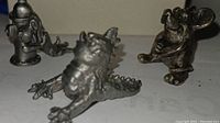 Four pewter miniature figurines shown together including a dog with fire hydrant, mouse, and spiked lizard, detailed close-up display.