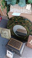 Photo showing large round mosaic mirror with green, brown, black sparkle tiles, 3 small wall plaques 'Laugh' and 'Love' visible, and medium decorative wood box.