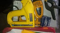 Yellow Stanley Bostitch electric staple tool and yellow Stanley electric staple/nail gun with staple boxes and black clamp in plastic bag