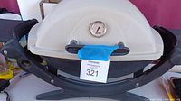 Front view of white-lid Weber portable propane grill with built-in thermometer, black base, and fold-out side tables.