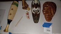 Wood masks, musical guiro, and wood nose glasses holder displayed on white surface with blue painter's tape