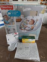 Photo of lot with Fisher-Price musical baby bouncer in box, bib, corner protectors and maternity seatbelt adjuster on table.