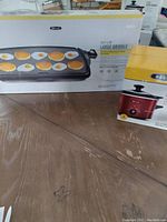 Photo showing boxed Bella large griddle and boxed Bella red crockpot on a wooden table