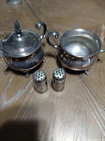 Silver plated creamer and sugar bowl along with silver plated salt and pepper shakers arranged on a wooden surface, visible tarnish on surfaces