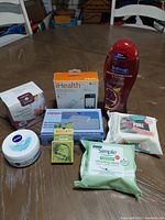Health and Beauty products on a wooden table including lotion, body wash, cleansing wipes, pill organizer, electronic health device box, and weight loss patches.