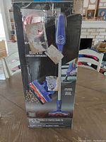 Box of Hoover Impulse cordless vacuum showing blue vacuum with roller brush head and slim metal rod.