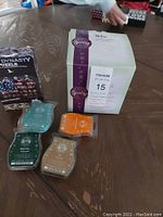 Photo of boxed Scentsy item with four wax bars in green, orange, blue, beige on wooden table beside a Dynasty puzzle box