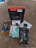 Wide view of phone accessories lot including camera lens kit box, Spigen Galaxy S7 Edge phone case box, two decorative phone cases, ProBuds earbuds box, and small black clip accessory in white box.