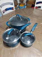 Three blue Rachel Ray pots with matching glass lids displayed on table