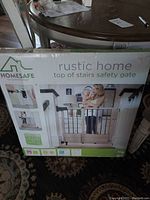 Front view of the Rustic Home baby gate in original box showing product image and branding details.