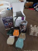 Lot items on wood table including open box, camo Scentsy warmer wrapped in plastic, six wax bars arranged in front, and Duck Dynasty puzzle box.