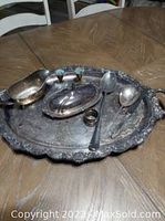 Silver plated lot showing large platter, gravy boat, spoons, covered dish, napkin ring, and brass candle sticks on wooden table