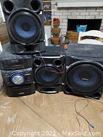 Sony stereo system main unit and three speakers on a wooden table with living room background.