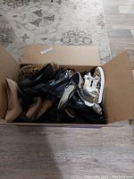 Box containing mostly black and beige dress shoes, flats and heels, and some sandals