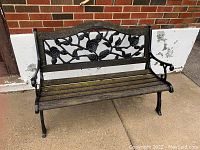 Front view of the garden bench showing wood slat seat and decorative cast metal floral backrest, weathered wooden top rail and legs.