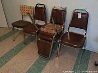 Five chairs consisting of four matching faux-leather chairs and one different fabric chair with chrome frames standing on a tiled floor.