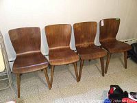 Four brown wooden chairs placed in a line against a wall on a patterned floor.
