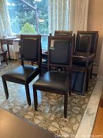 Six black leather dining chairs grouped together showing front and back views on tiled floor.