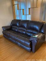 Full view of the brown leather three-seat couch with visible padded cushions and armrests.