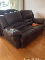 Front and angled view of the brown leather two-seat couch with leather care kit on the seat.