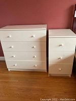Photo showing two white dressers side by side against a red wall on wooden floor.