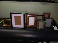 Photo showing nine assorted picture frames in various sizes and materials arranged on a black surface against a green background
