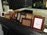 Wide shot showing collection of 12 assorted picture frames on black surface with some framed prints inside.