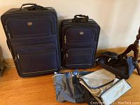 Two wheeled navy blue suitcases side by side with three carry bags arranged on the floor including striped tote, black soft bag, and small black/gray bag.
