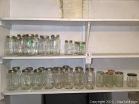 Shelf showing an assortment of 33 clear glass mason jars of different sizes, all with metal lids. Jars are empty and appear to need cleaning.