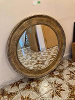 Framed circular mirror leaning against wall on tiled floor, showing full front view.