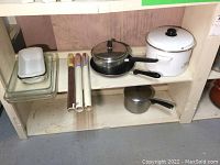 Shelves with six pots with lids, pan, two mixing bowls, three glass baking dishes and some rolls of plastic wrap.