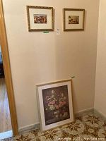 Wide shot showing two smaller framed cherub prints hung on the wall and one large floral print leaning against the wall on the floor.