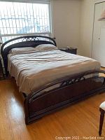 Complete view of the bed with mattress showing wooden headboard with curved arch decorative pattern and footboard in dark wood finish.
