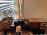 Wide view showing Harman Kardon receiver with two Panasonic speakers and a cardboard box containing cables and accessories on a table.