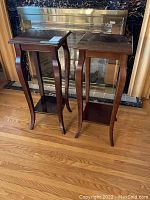 Pair of small wood tables or plant stands with curved legs in front of a fireplace, showing overall condition and style.
