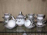 Full view of tea set including eight cups stacked on saucers and the central teapot.