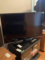 Samsung 37 inch screen TV mounted on a black pedestal stand with remote control on the stand.