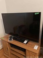 Insignia flat screen TV on wooden stand with remote control placed on top, showing full unit setup and included remote.